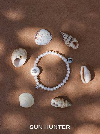 SUN HUNTER unique pearl bracelet displayed among seashells on a sandy surface