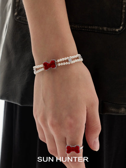Sun Hunter velvet bow pearl bracelet displayed on a model's wrist, featuring a striking red bow design