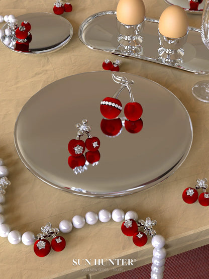 Elegant velvet cherry stud earrings by SUN HUNTER displayed elegantly on a reflective plate