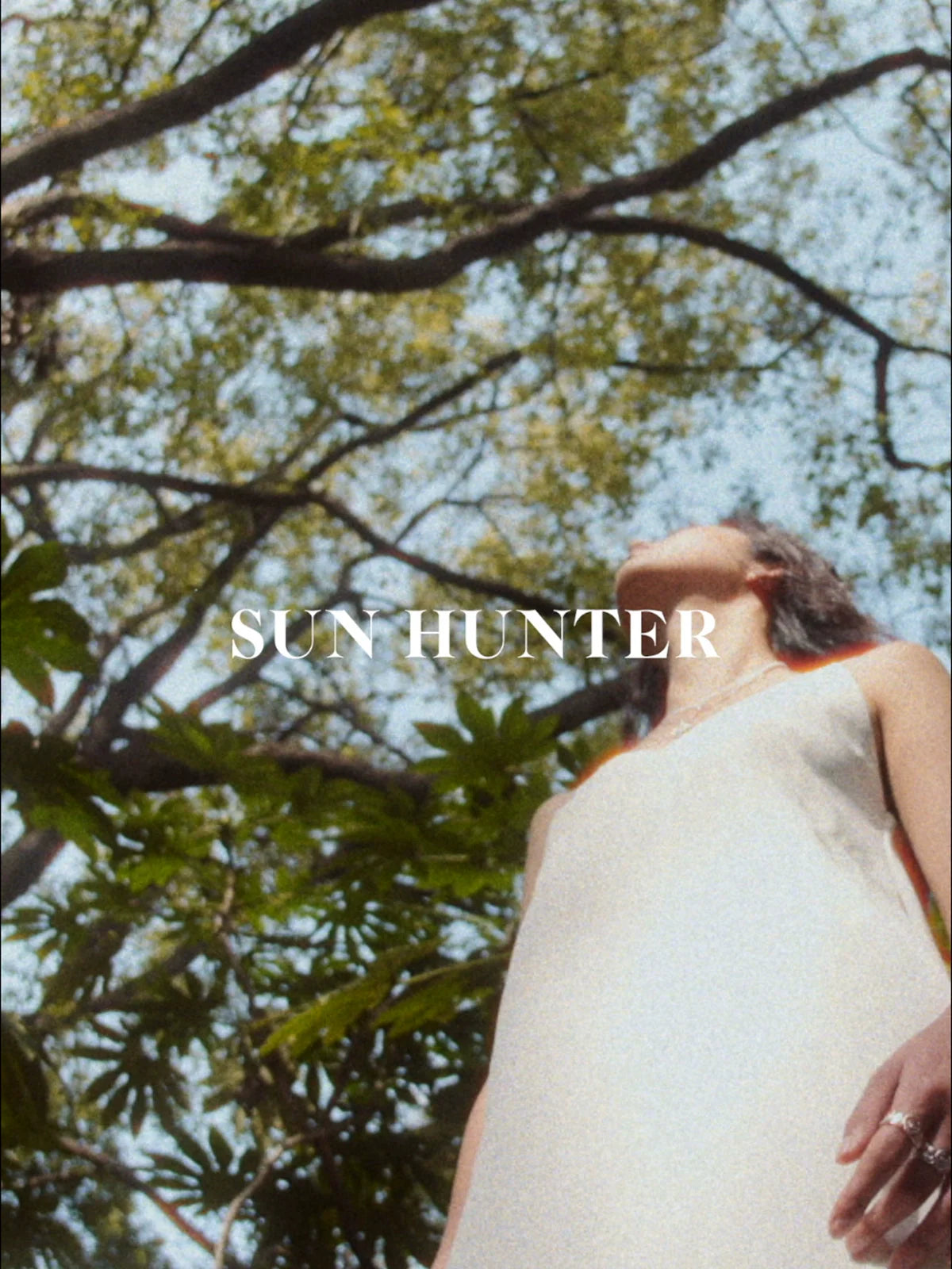 Model wearing a delicate dress showcasing the SUN HUNTER love lock chain ring under lush green trees